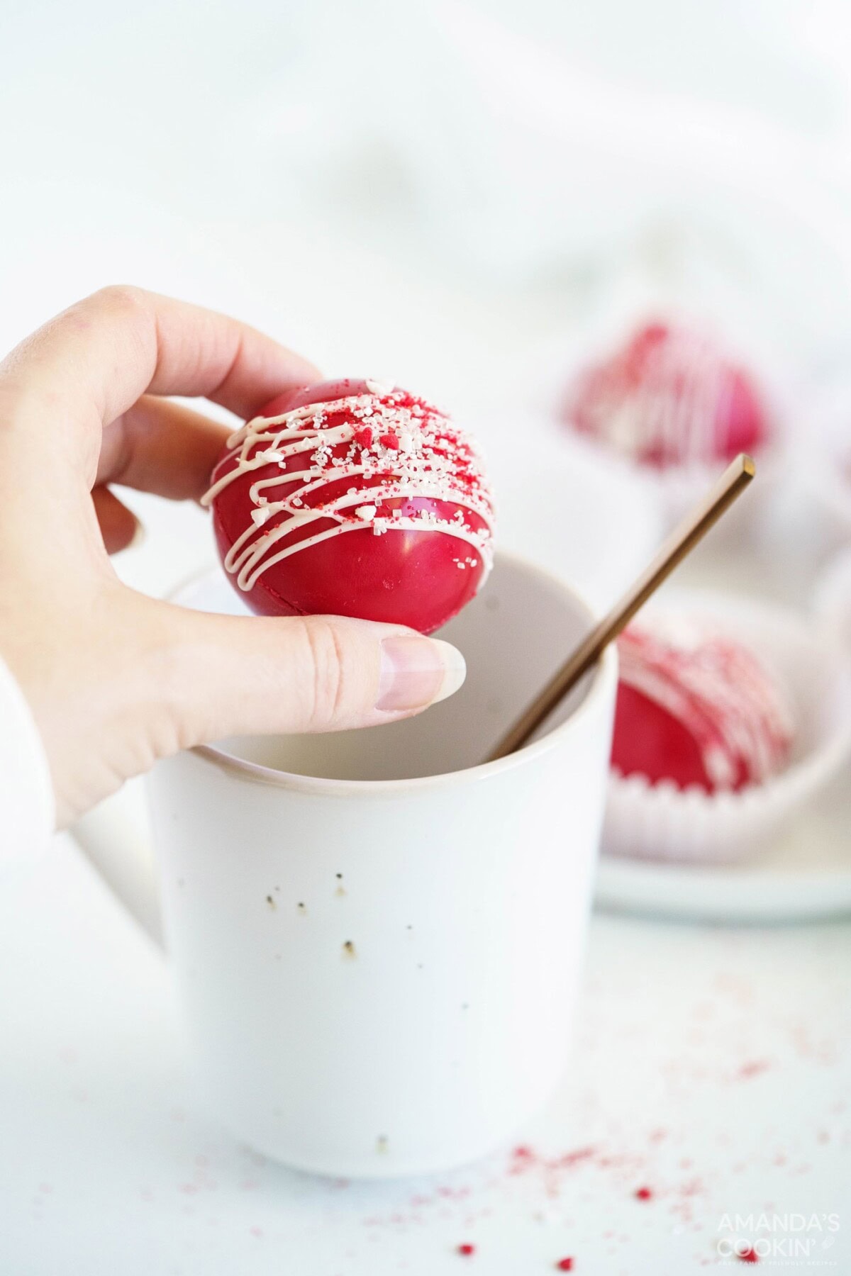 woman holding red velvet cocoa bomb over mug