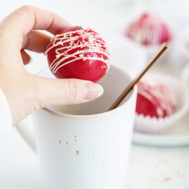 woman holding red velvet cocoa bomb over mug