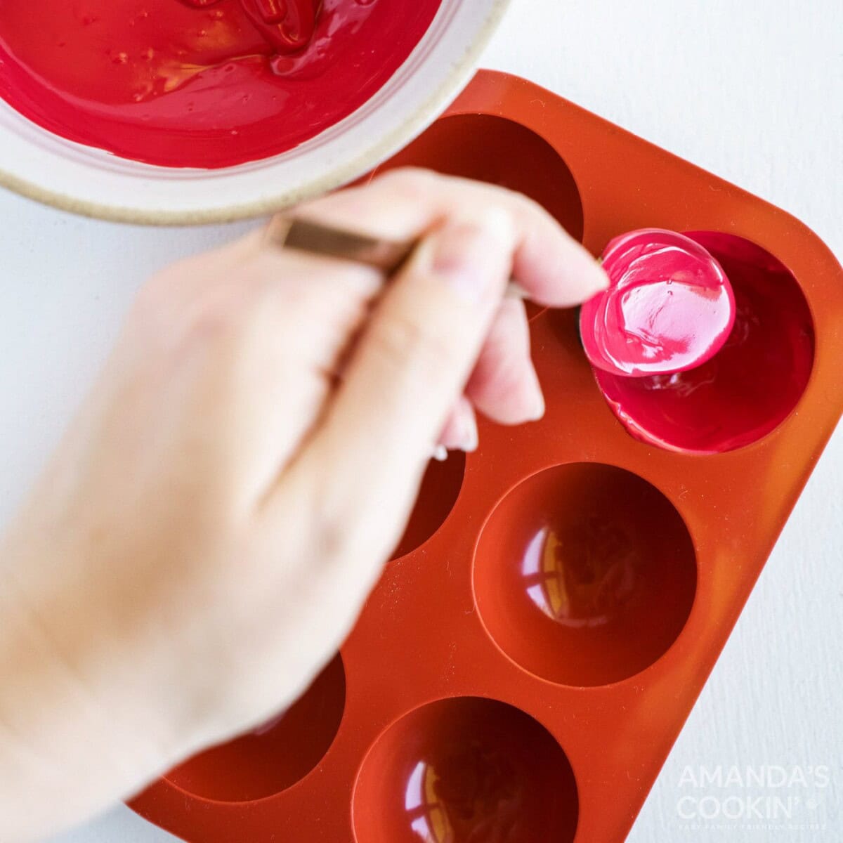 spooning melted red candy into cocoa bomb molds