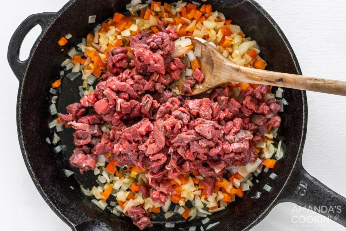 chopped steak on top of veggies in cast iron skillet