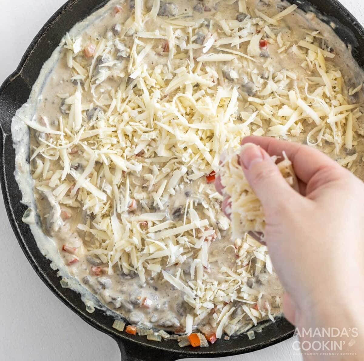 topping Philly cheesesteak dip with cheese in a skillet