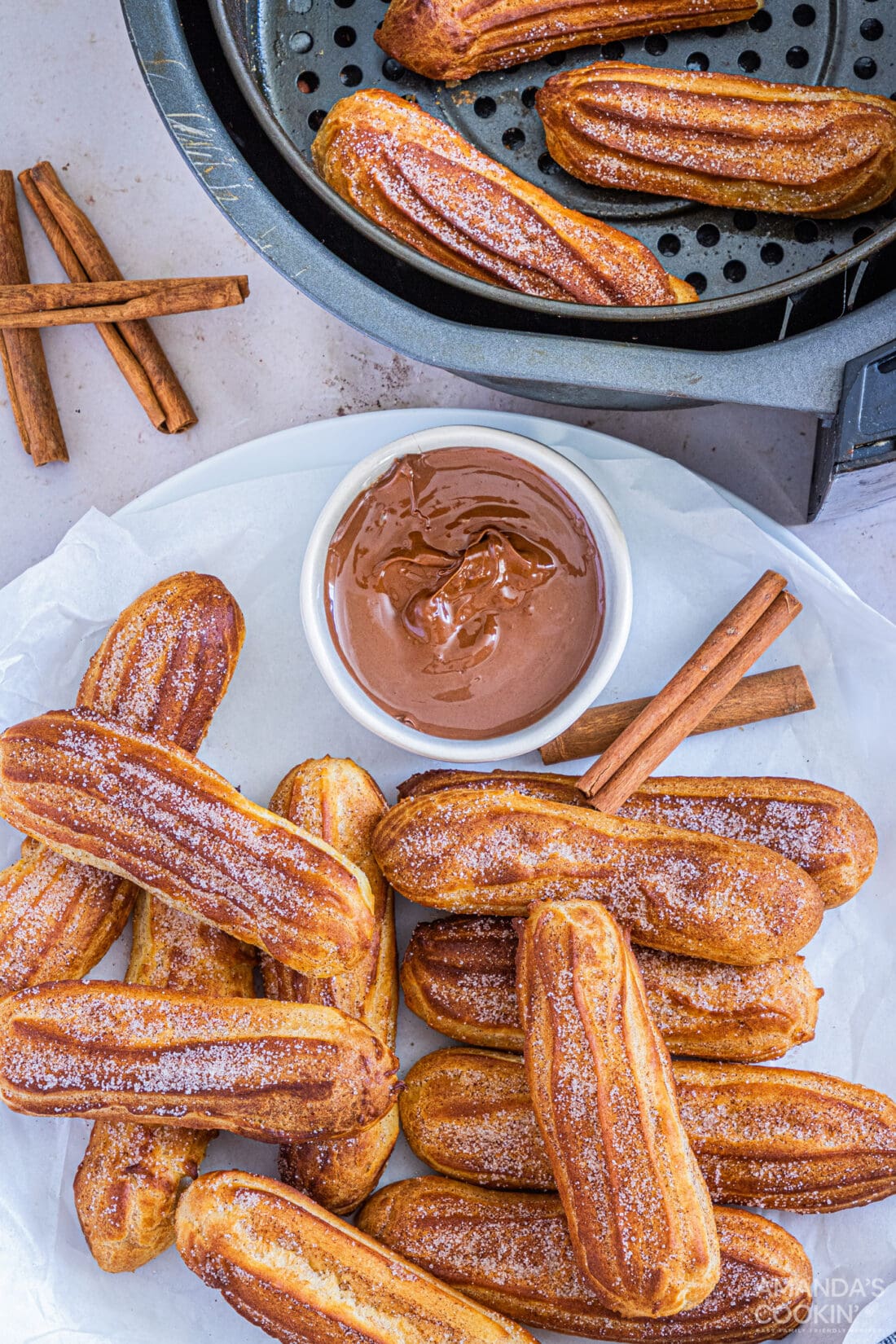 plate of Air Fryer Churros sitting by an air fryer basket with more churros