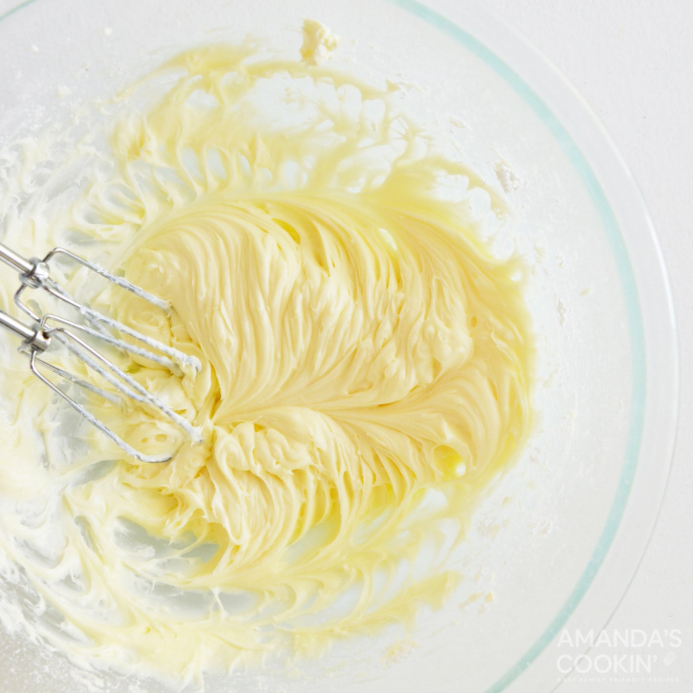 beating cream cheese frosting with a handheld mixer