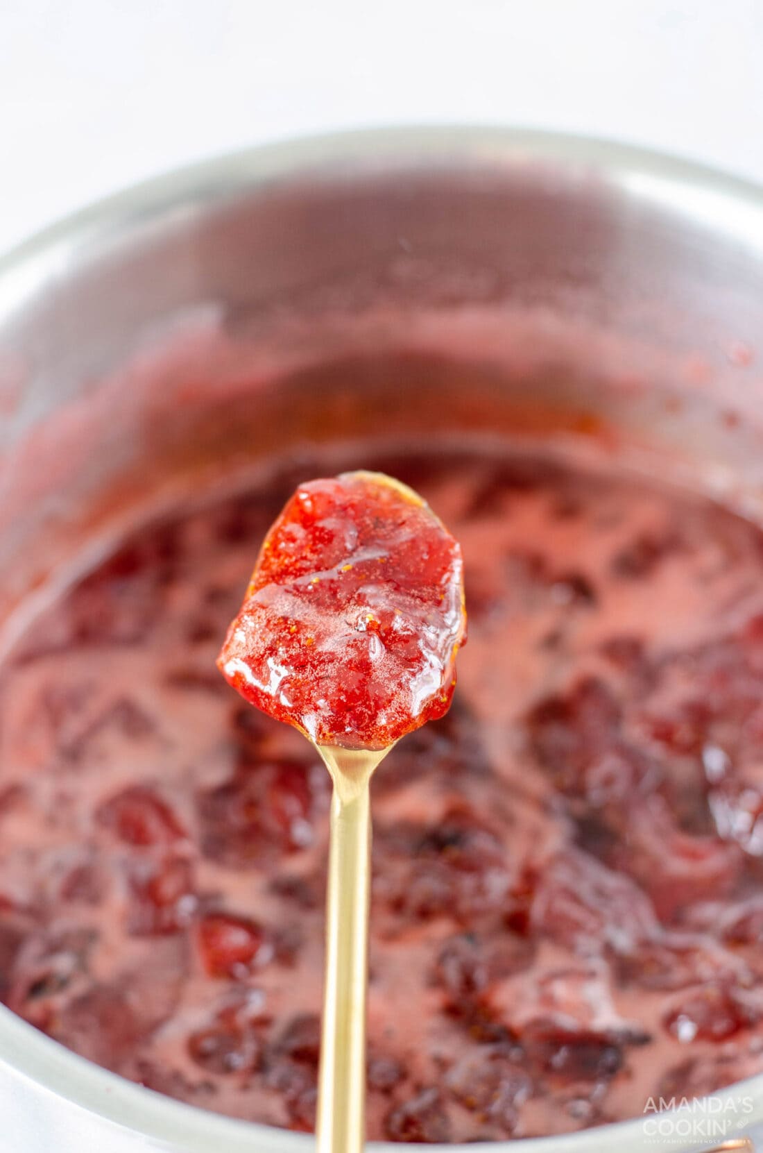 spoon lifting strawberry jam from saucepan