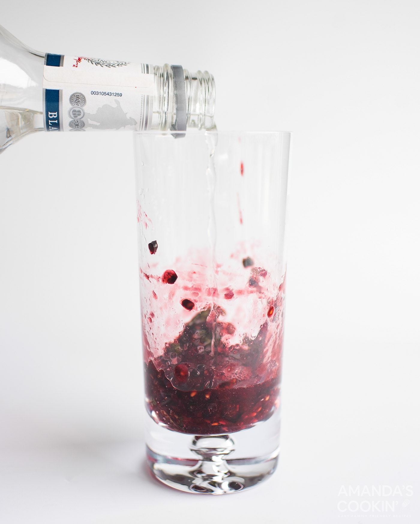Pouring rum into muddle blackberries and mint in a glass