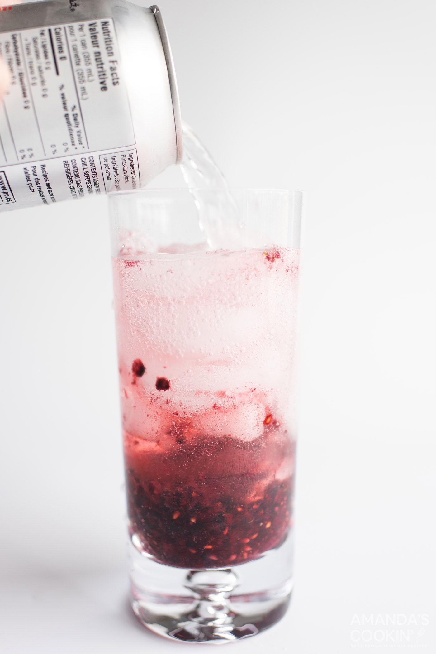 pouring club soda into a glass of blackberry mojito