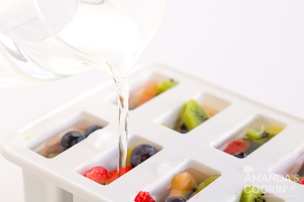 pouring white juice over fruit in popsicle mold