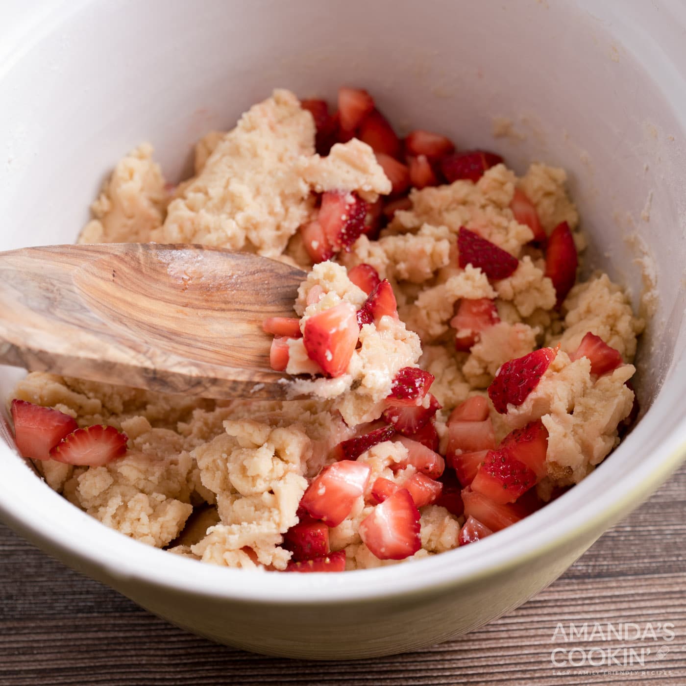 wooden spoon folding strawberries into cookie dough