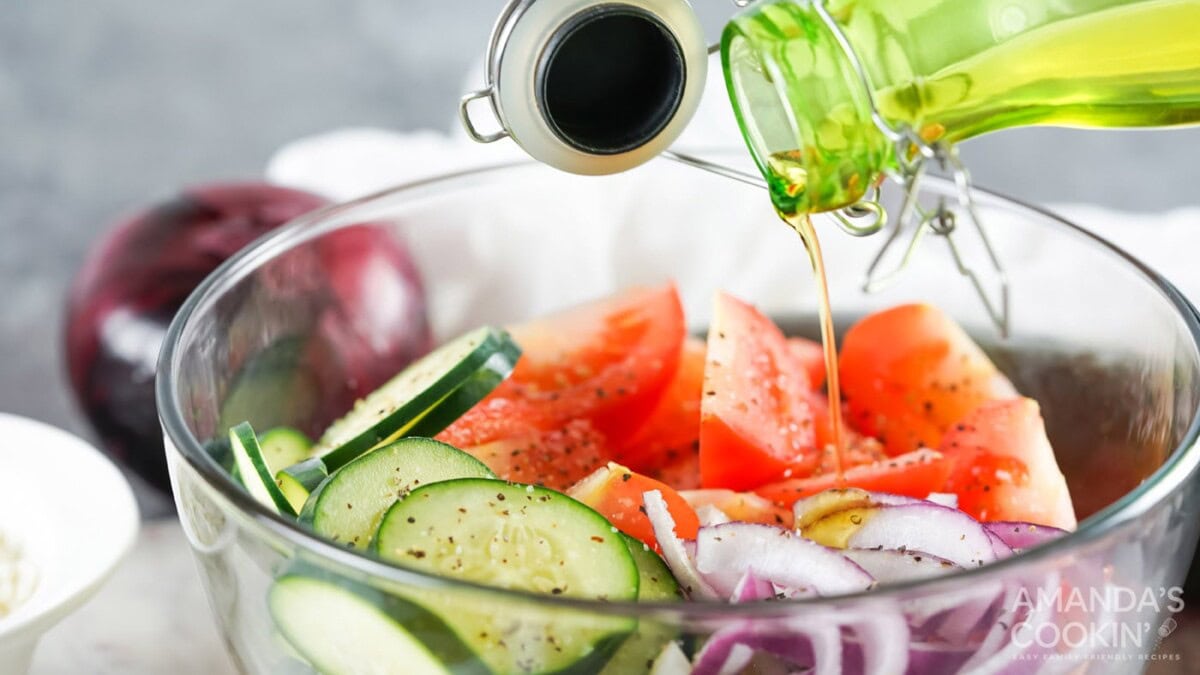 pouring olive oil into cucumber, tomato, and onion salad