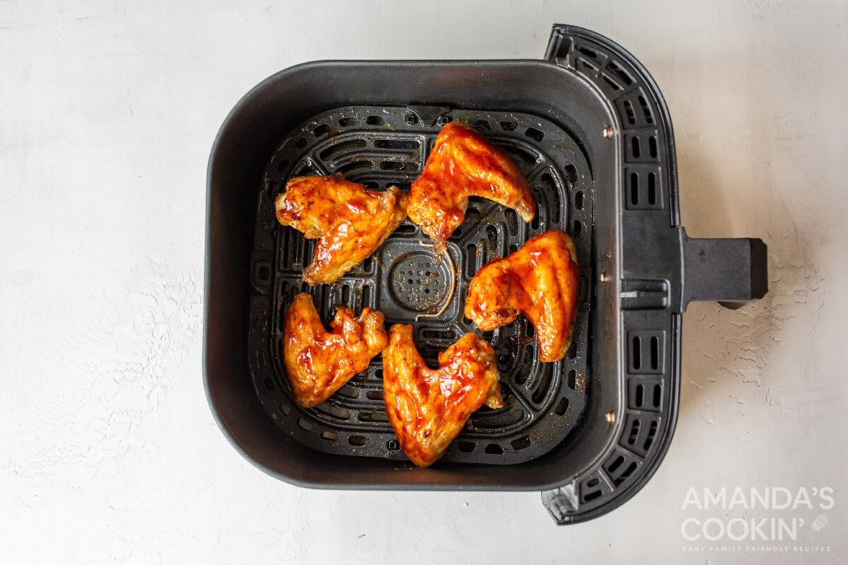 chicken wings in air fryer basket with sauce