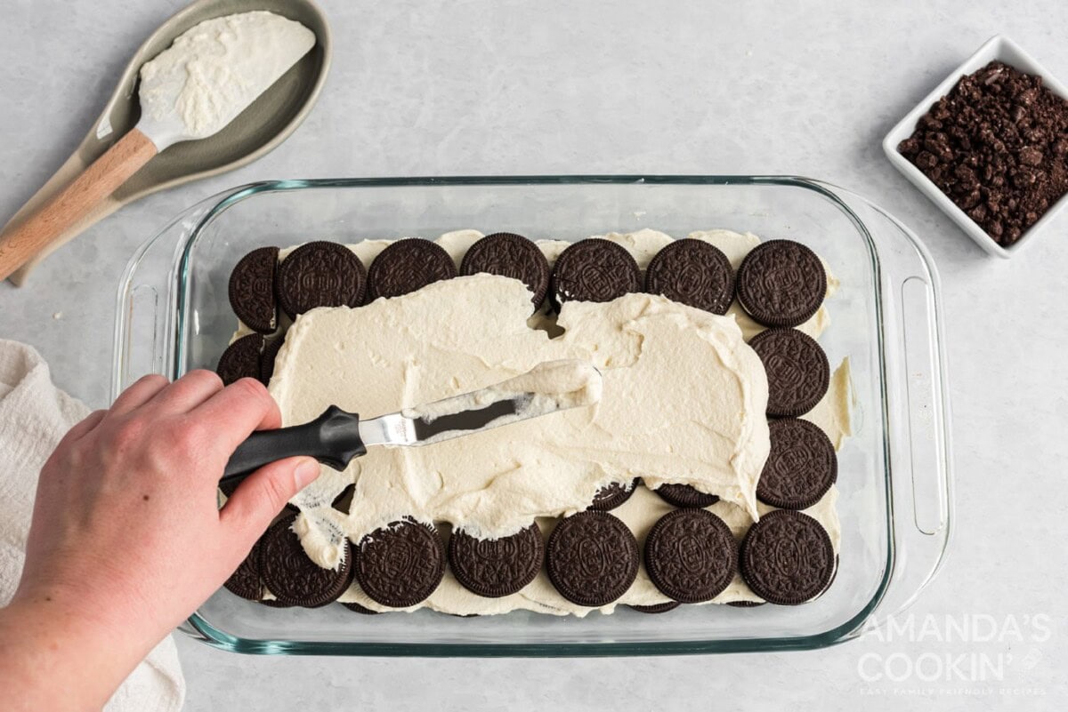 spreading whipped topping over the top of oreos in a baking dish