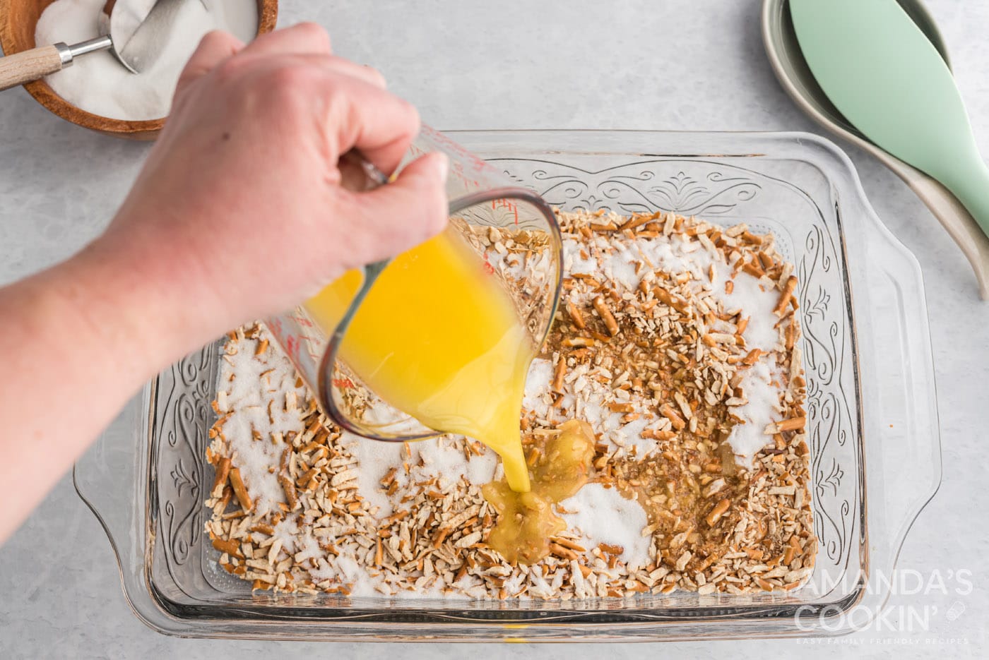 adding melted butter to pretzels and sugar in a baking pan