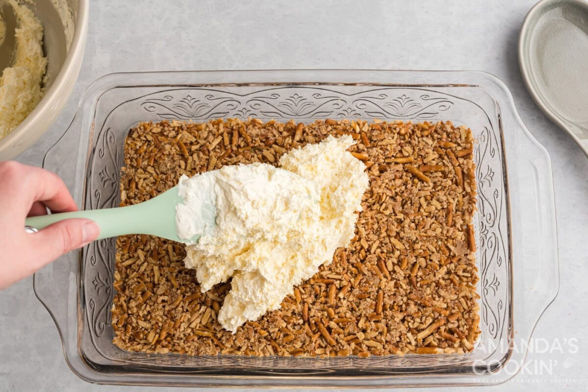 spreading cream cheese layer on top of a pretzel crust