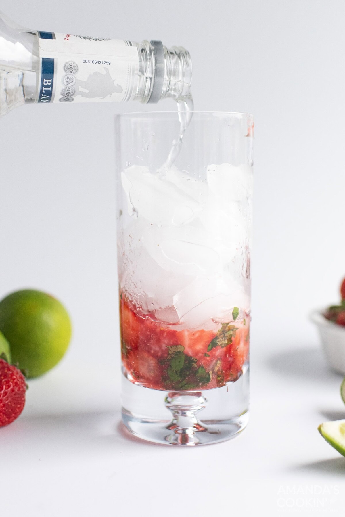pouring club soda into highball glass with strawberries and mint