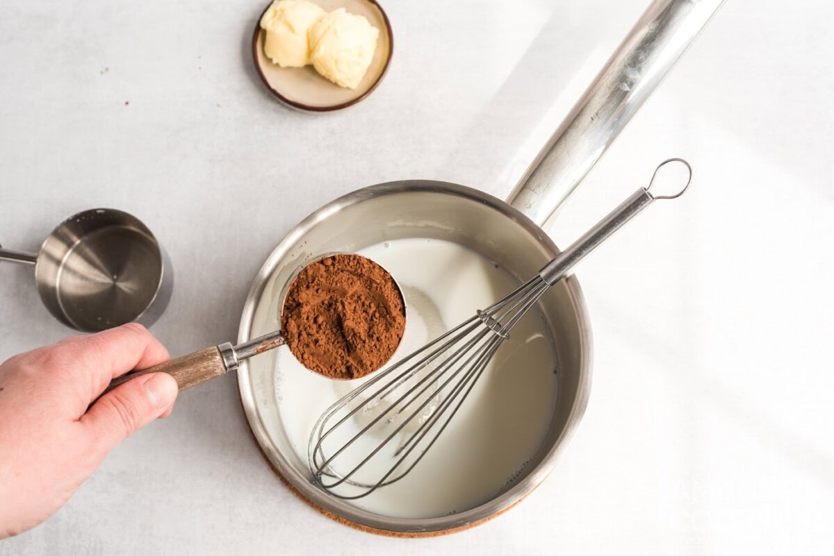 cocoa in measuring cup over saucepan of milk and sugar