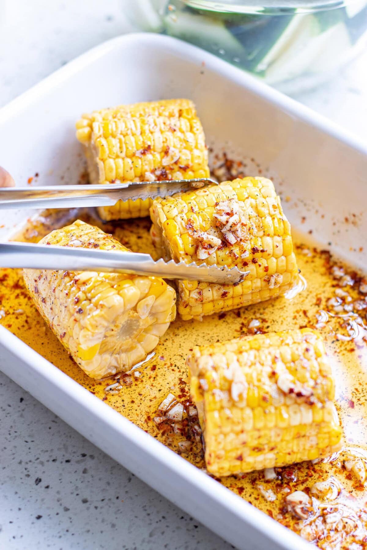 tongs holding marinated corn on the cob