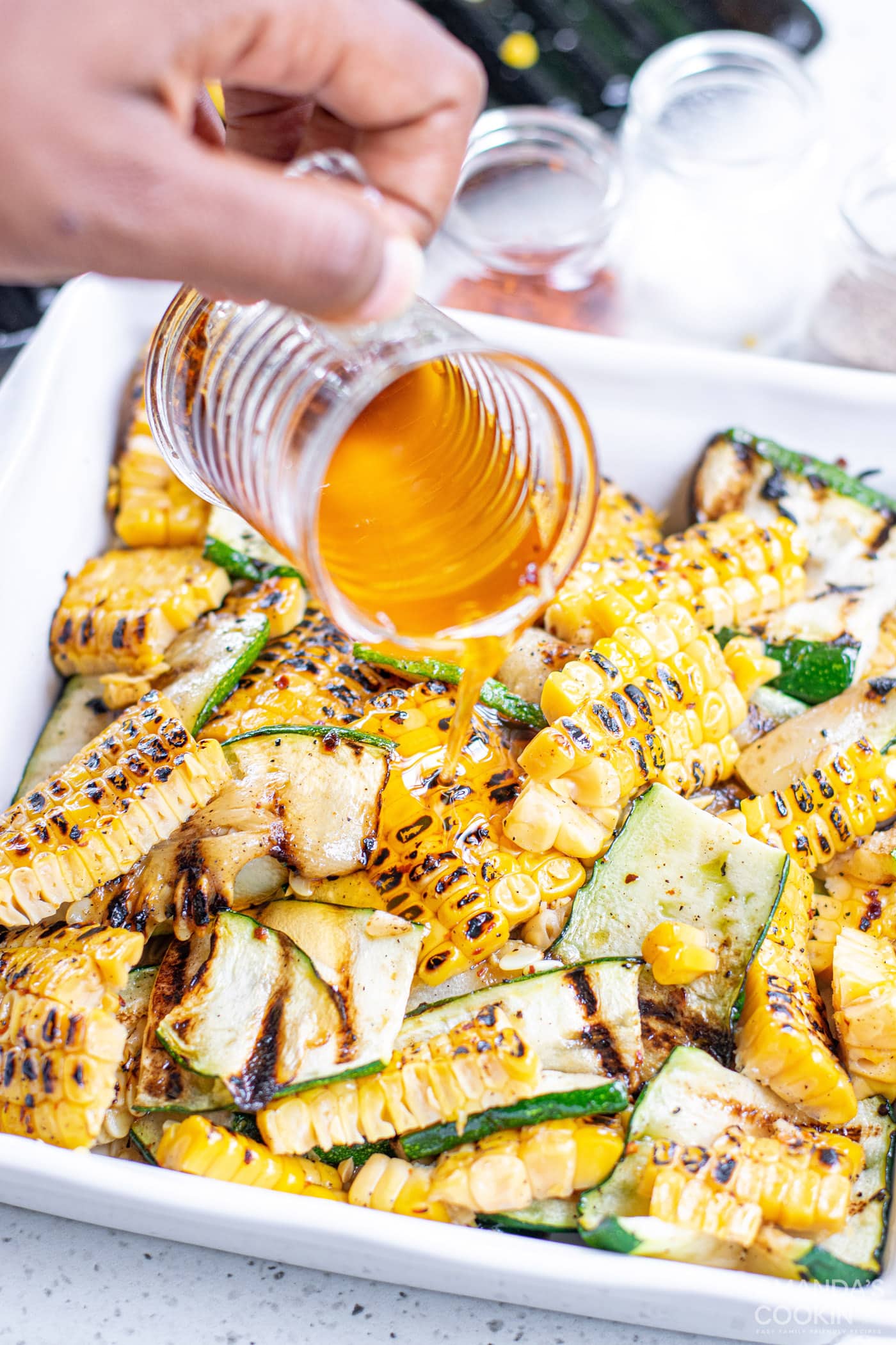 adding olive oil to grilled corn and zucchini salad with feta