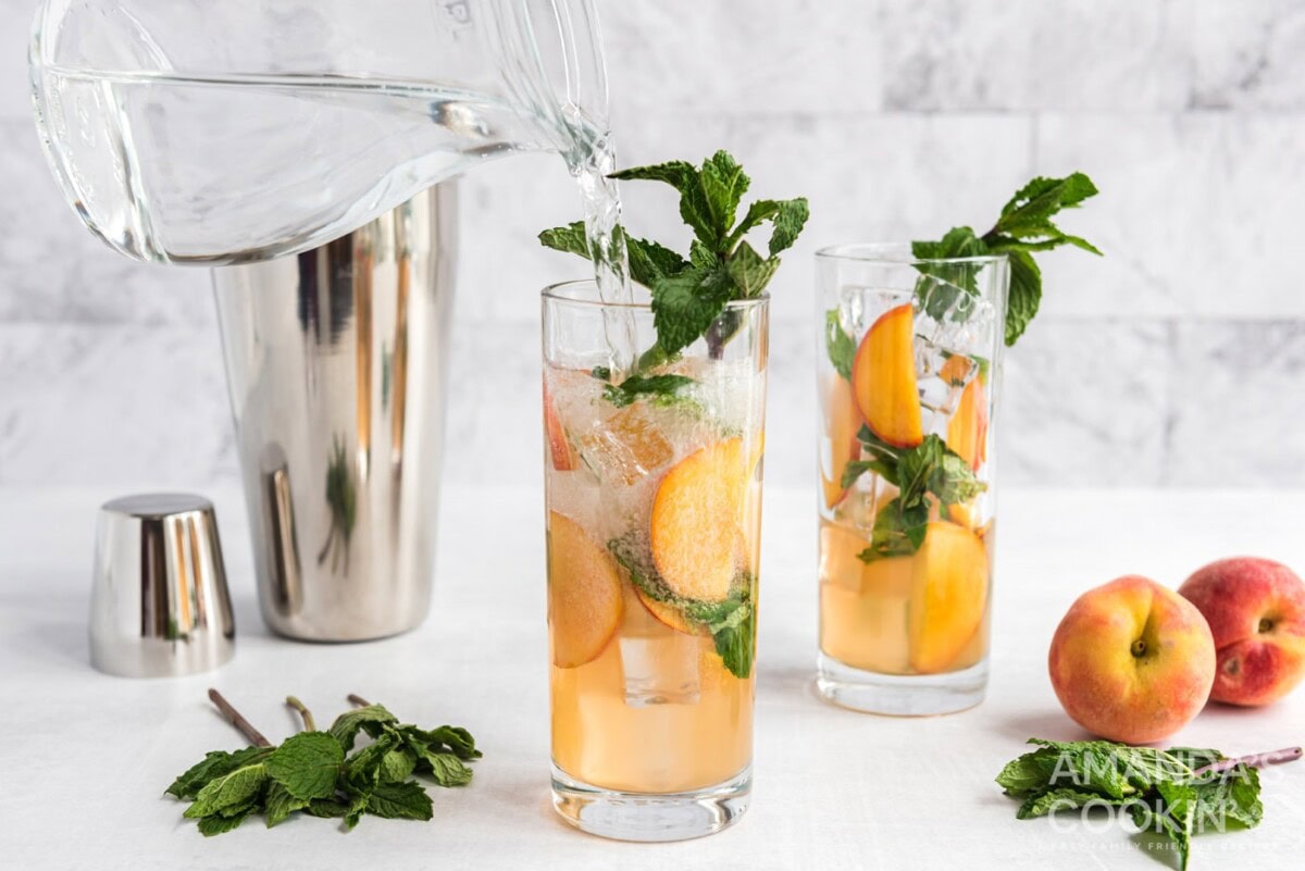 adding club soda to peach mojito in glass