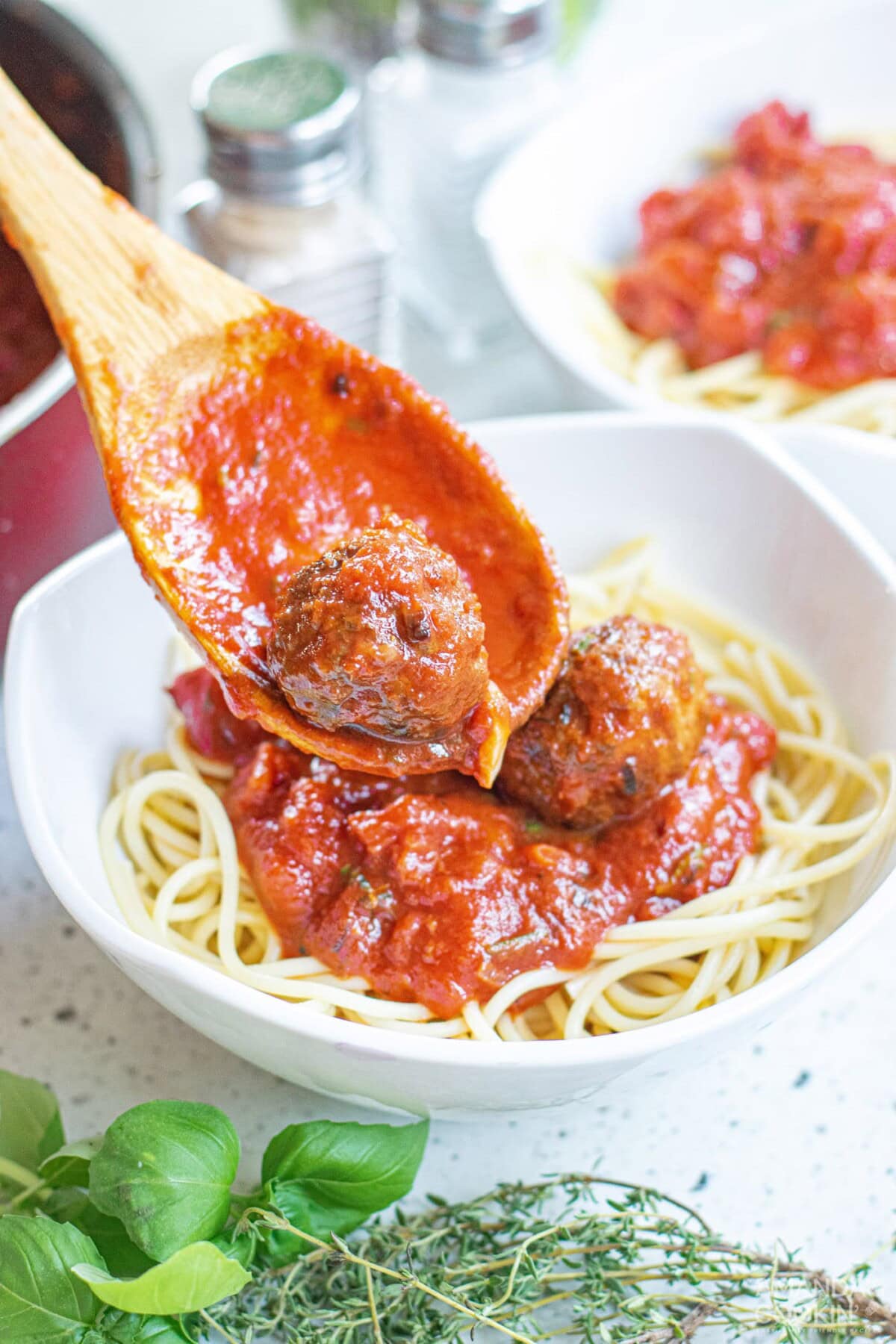 spooning meatballs and marinara over spaghetti noodles