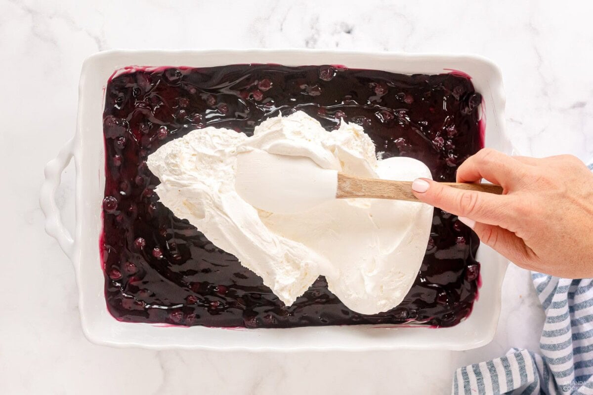 spreading whipped topping on top of blueberry pie filling