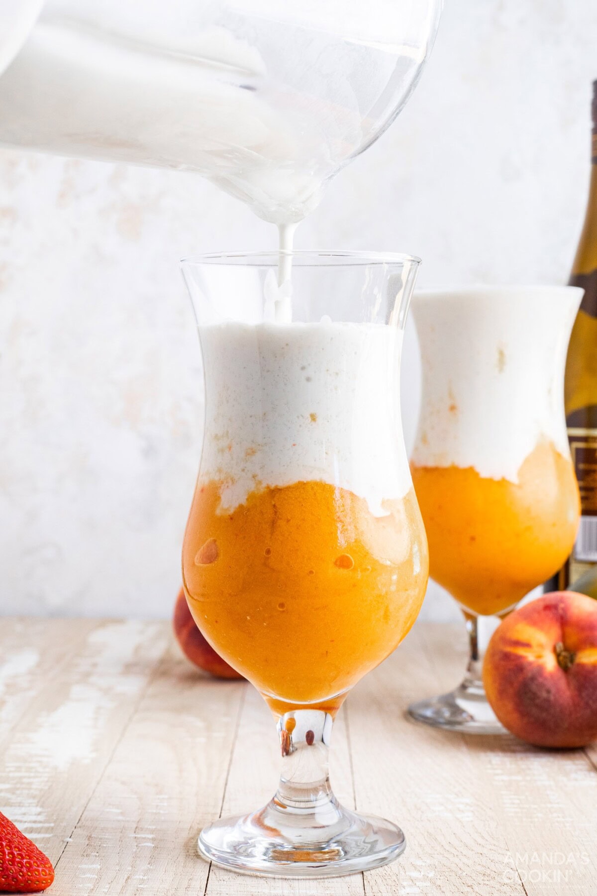 pouring coconut cream slush into fruit slush in a glass