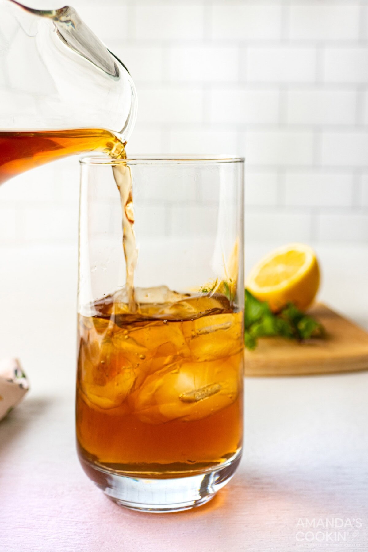 pitcher pouring iced tea into tall glass with ice