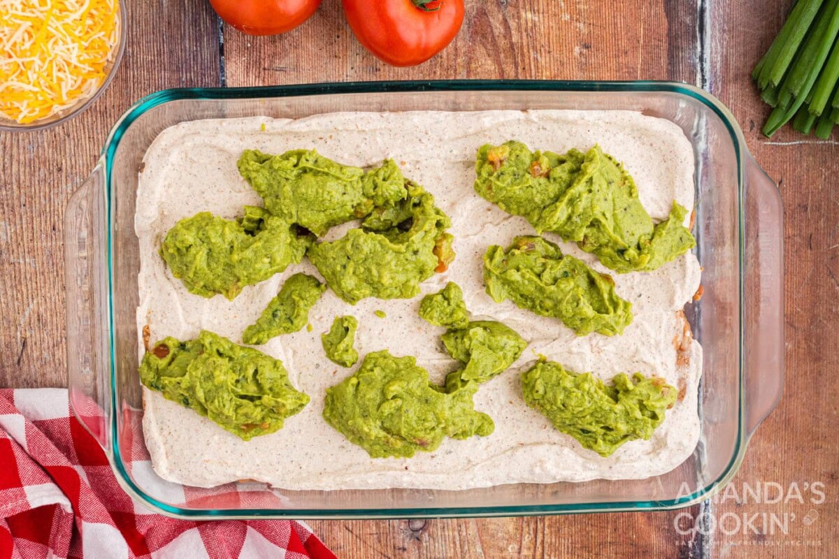 dollops of guacamole on top of sour cream and cream cheese in a dish