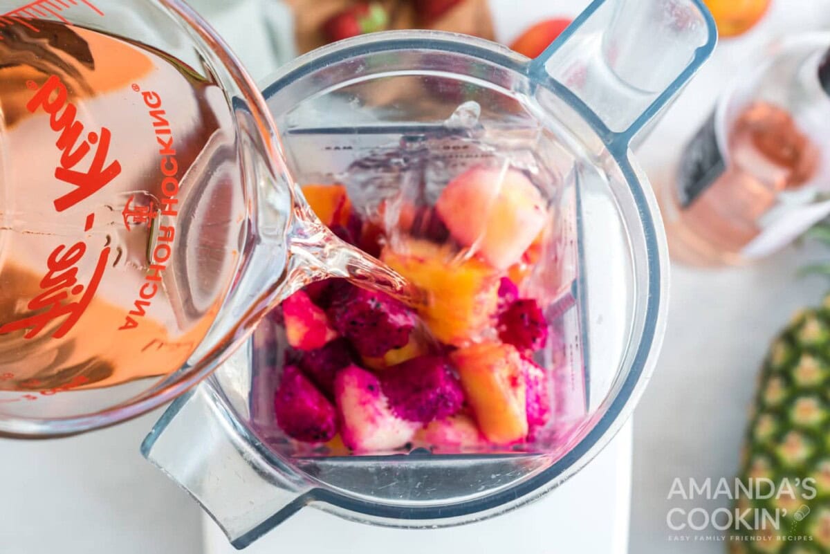 pouring rose wine into a blender with fruit