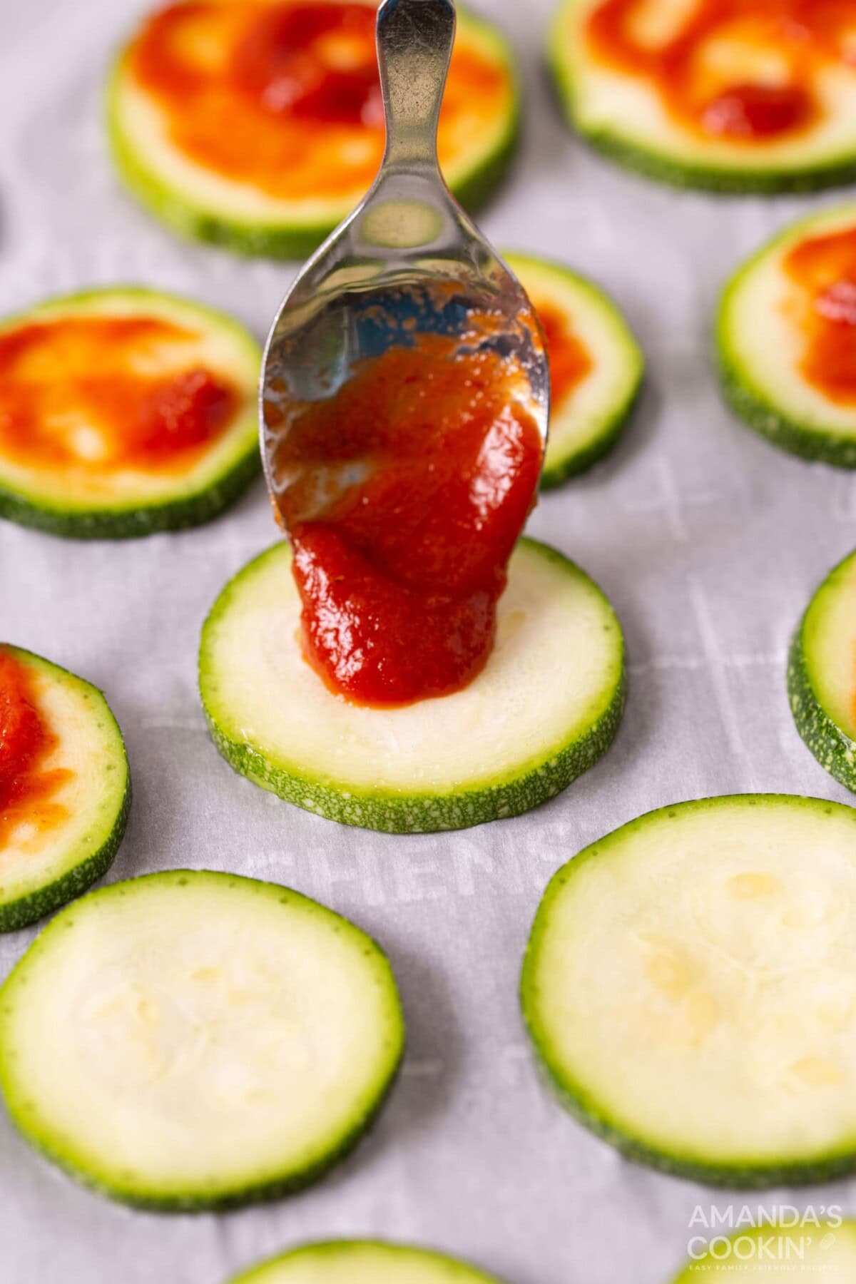 spoon pouring pizza sauce onto zucchini slice