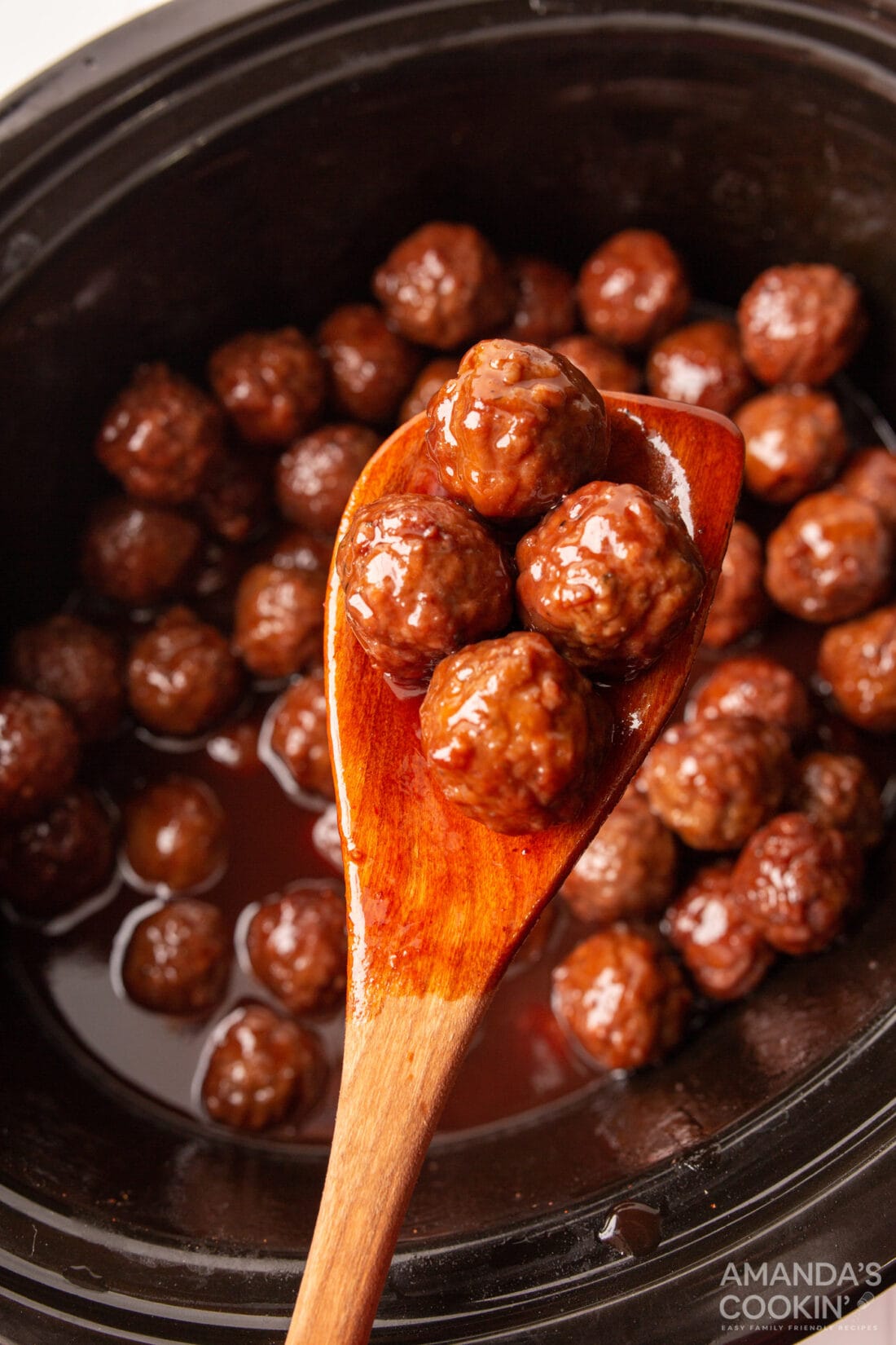 lifting appetizer meatballs from crockpot with wooden spoon