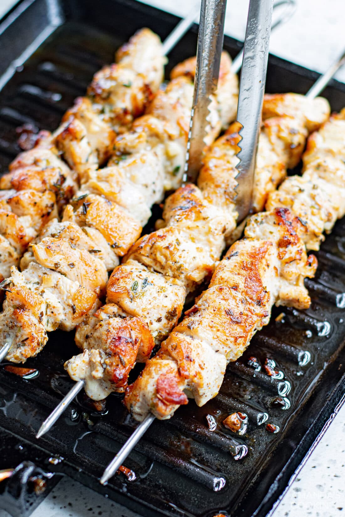 lifting Greek Chicken Kabobs off grill with tongs