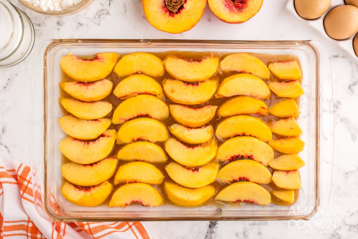 peach slices on top of butter and brown sugar mixture in a baking dish