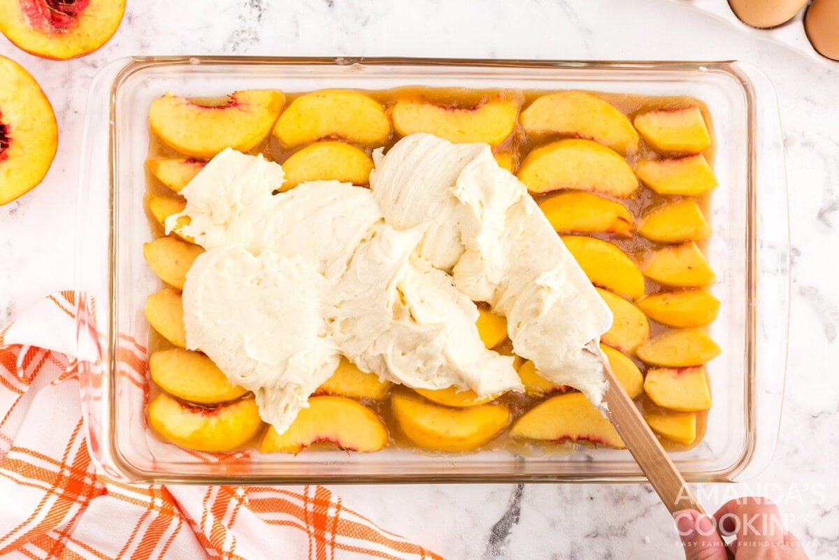 spread cake batter on top of peaches in a baking dish