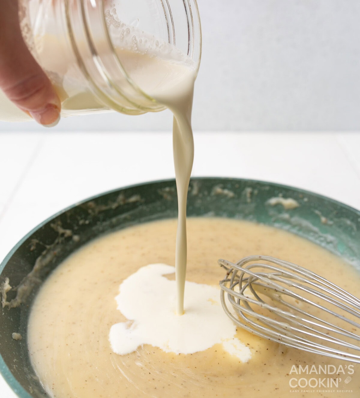 pouring heavy cream into cream of chicken soup over a skillet