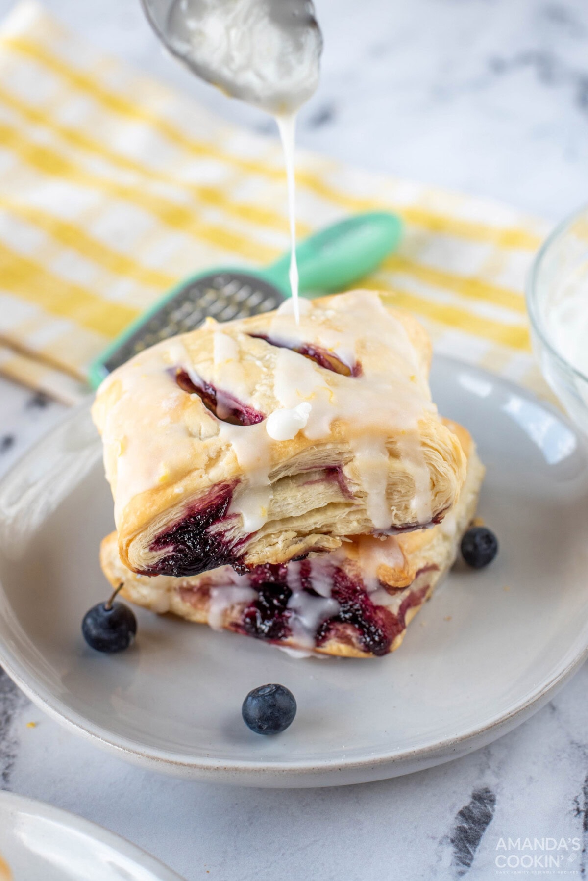 drizzling glaze onto a stack of Lemon Blueberry Croissant Hand Pies