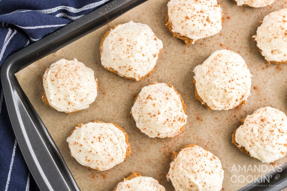 cream cheese frosting on top of pumpkin cake mix cookies on a baking sheet