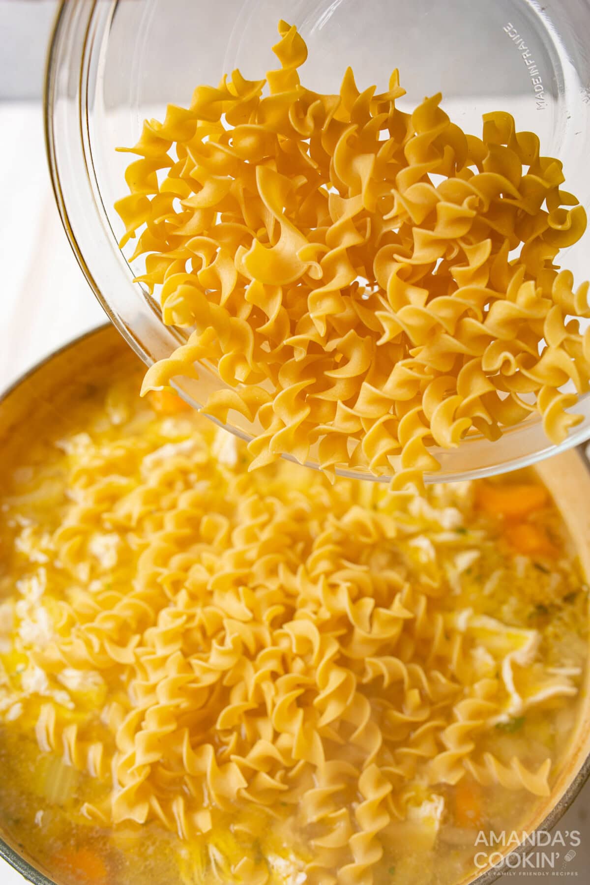 pouring egg noodles into chicken noodle soup broth