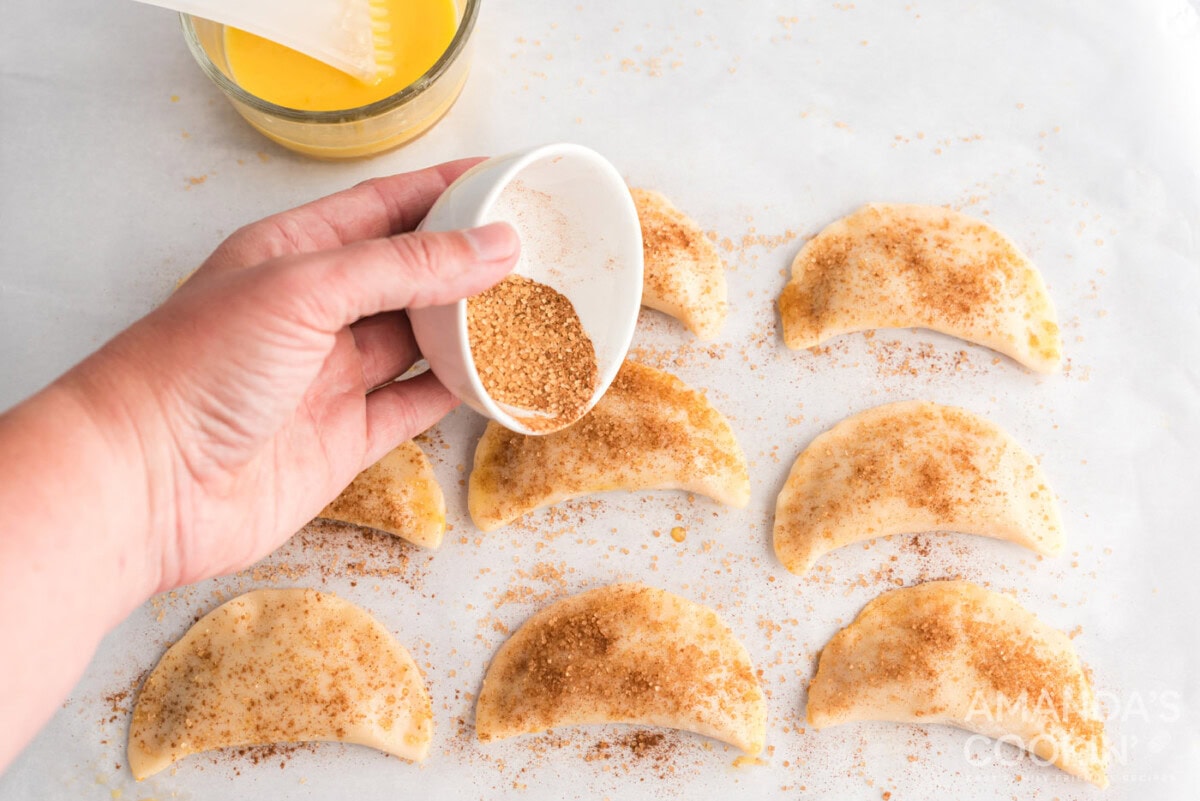 sprinkling cinnamon sugar on top of pumpkin hand pies