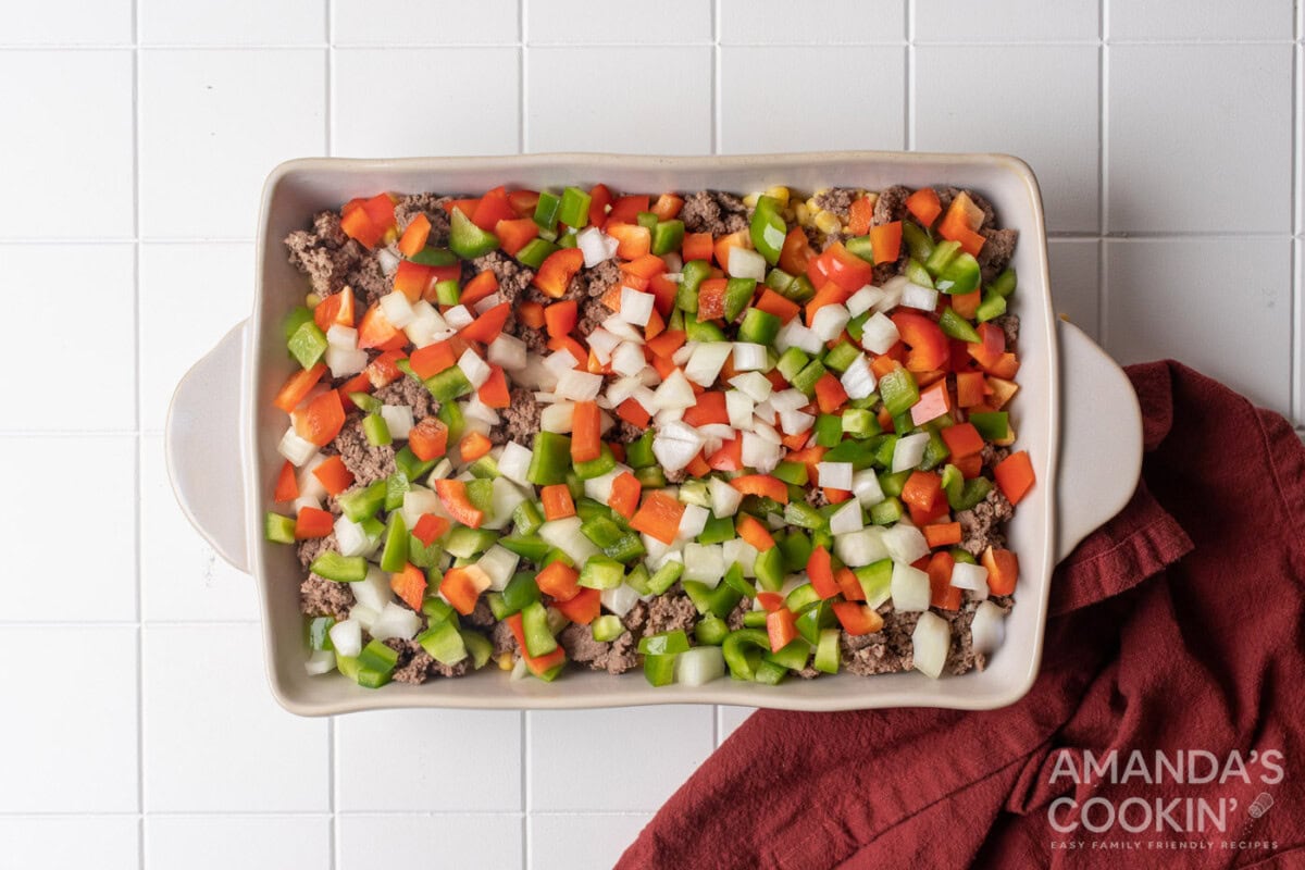 chopped peppers and onion on top of ground beef in a baking dish