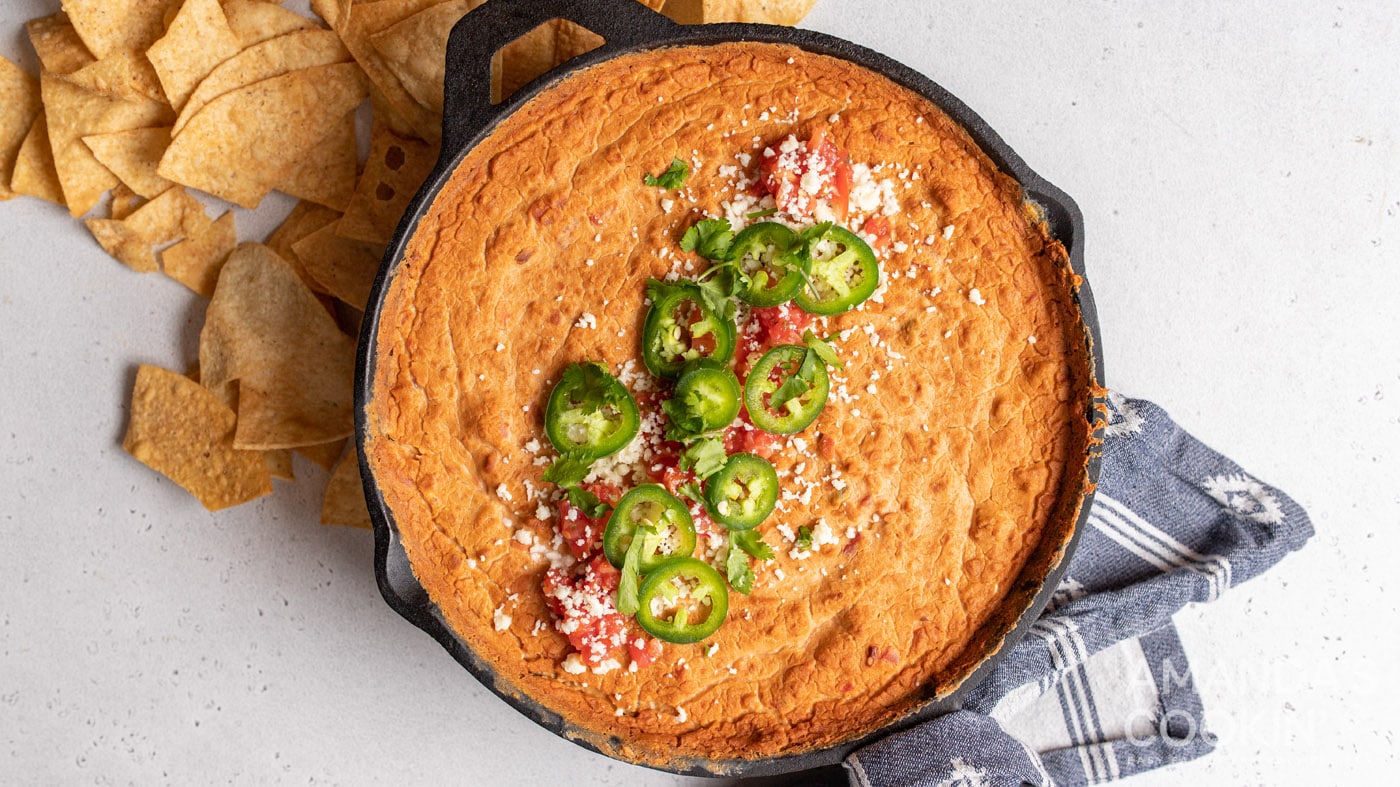 Refried beans, tomatoes, jalapenos, taco seasoning, cream cheese, and sour cream make this bean dip 