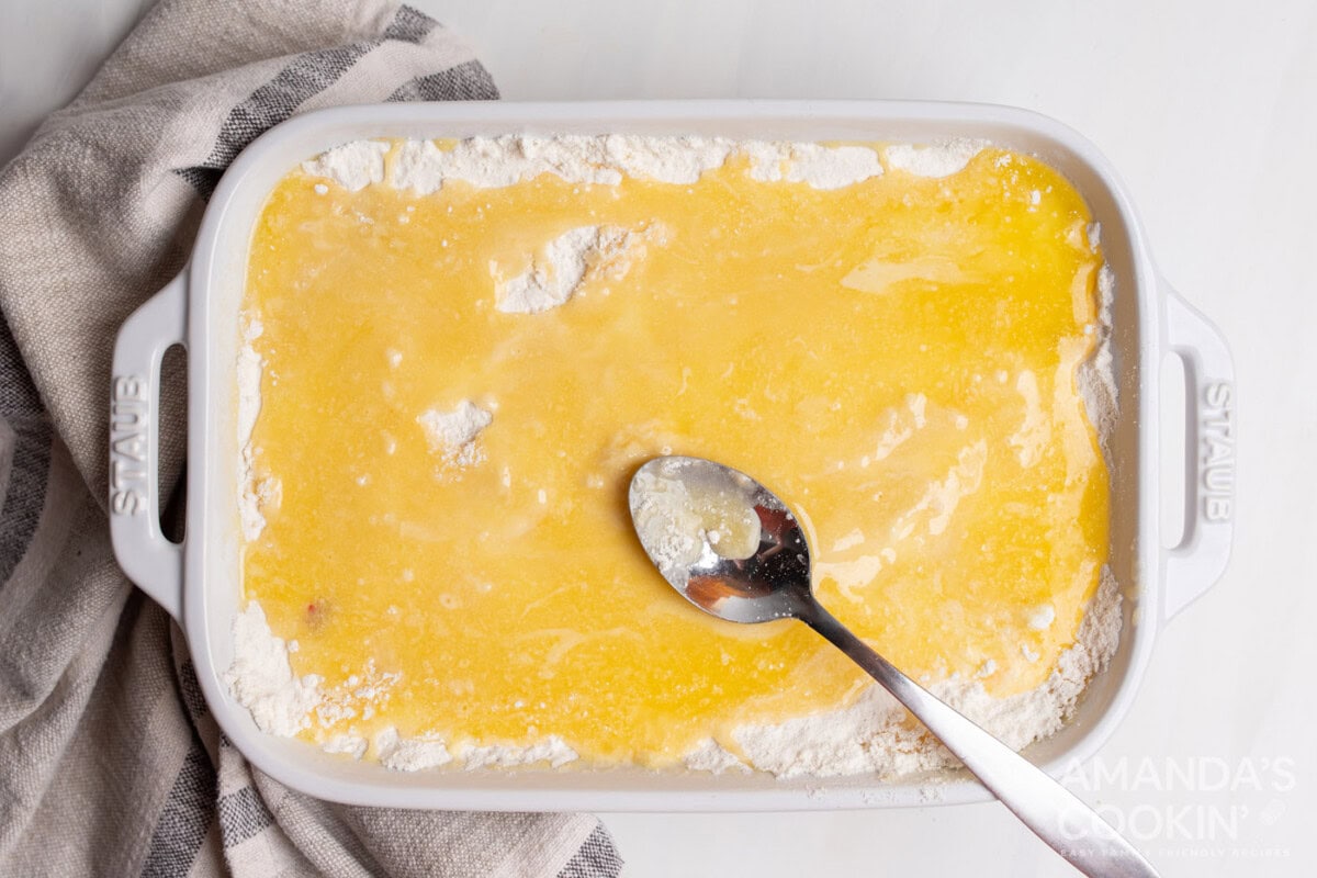 spooning butter over cake mix in a casserole dish
