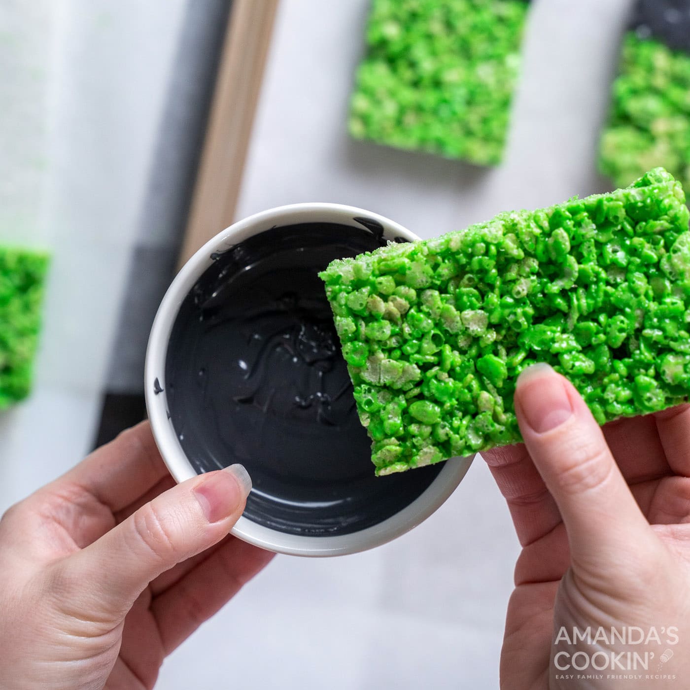 hand dipping green rice krispie treat into candy melts