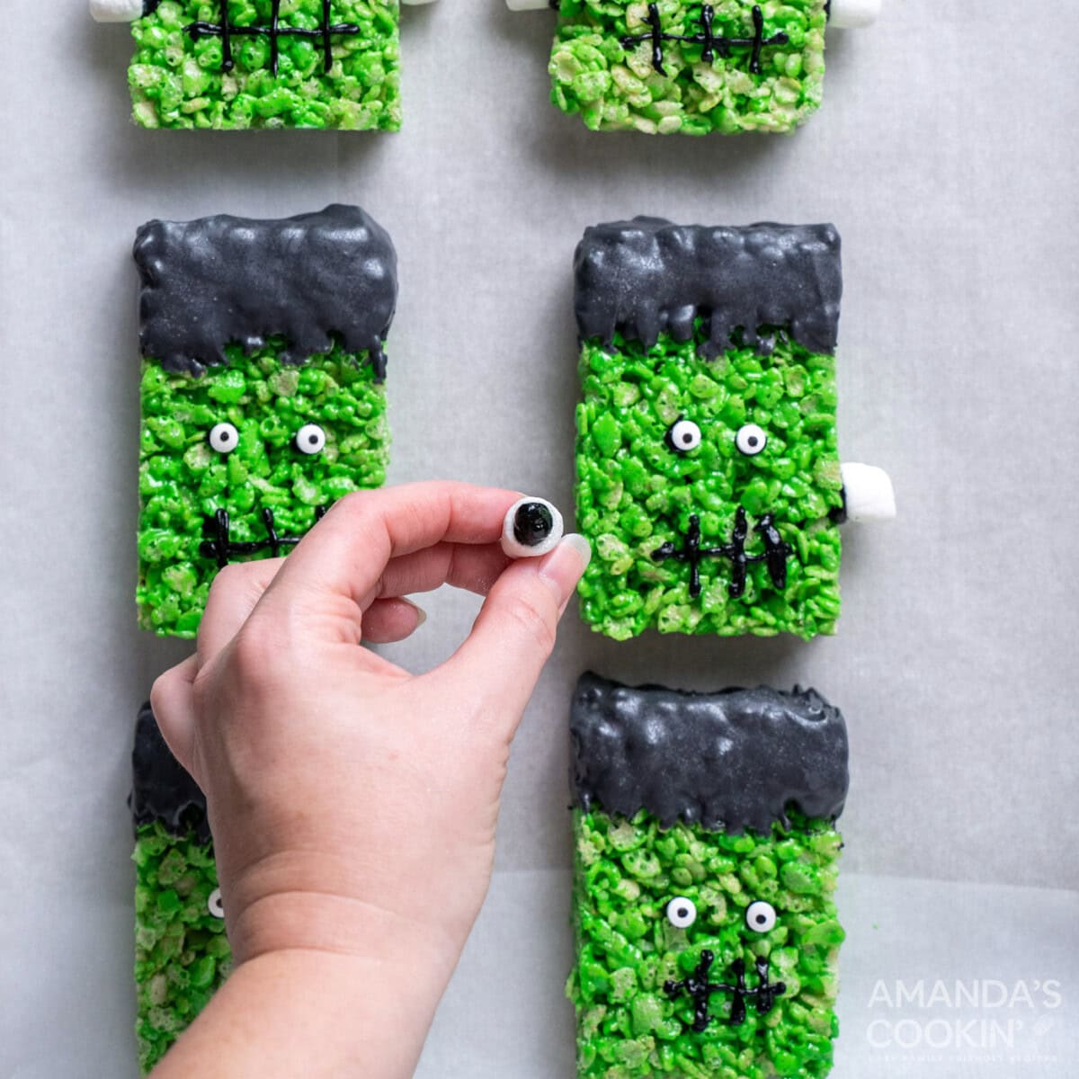 hand attaching mini marshmallows to frankenstein rice krispie treats