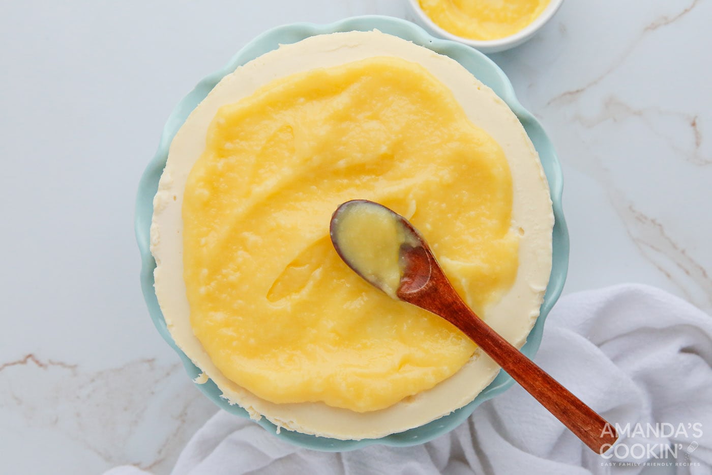 spoon spreading lemon curd on top of cheesecake