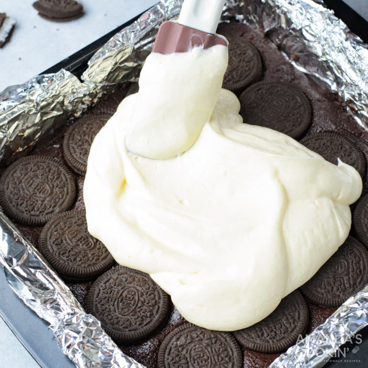 spatula smoothing out cheesecake layer on top of oreo brownies