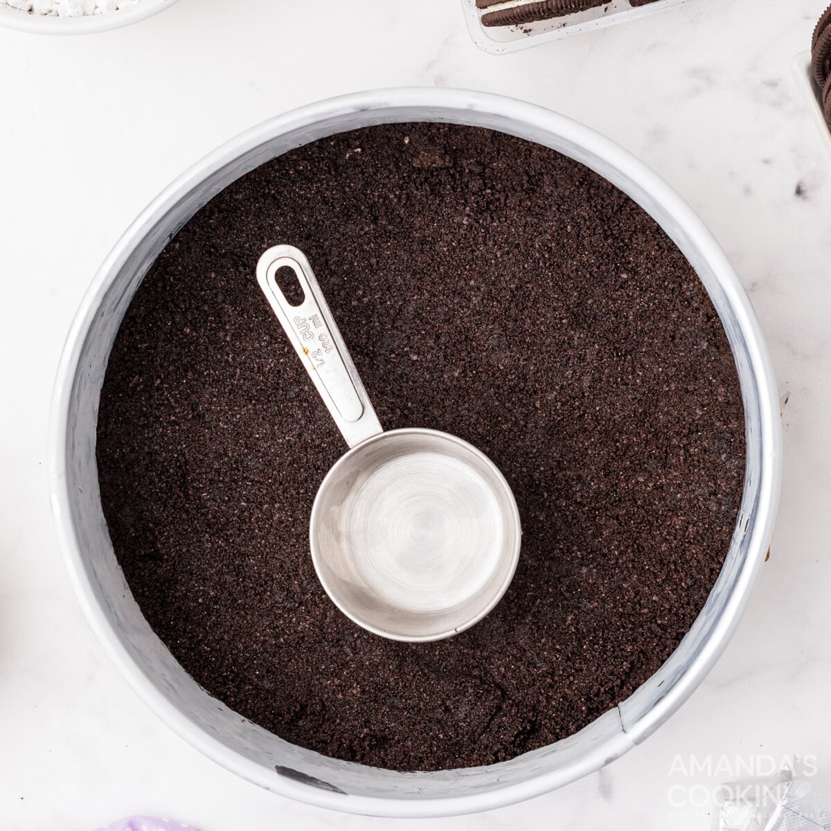 measuring cup pressing down oreo crumbs to make a crust