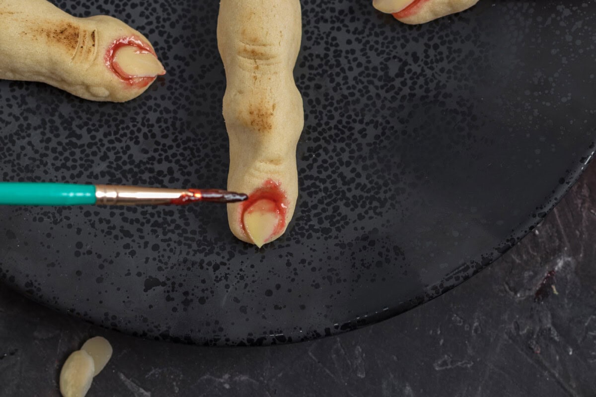 painting strawberry jam on witch finger cookies