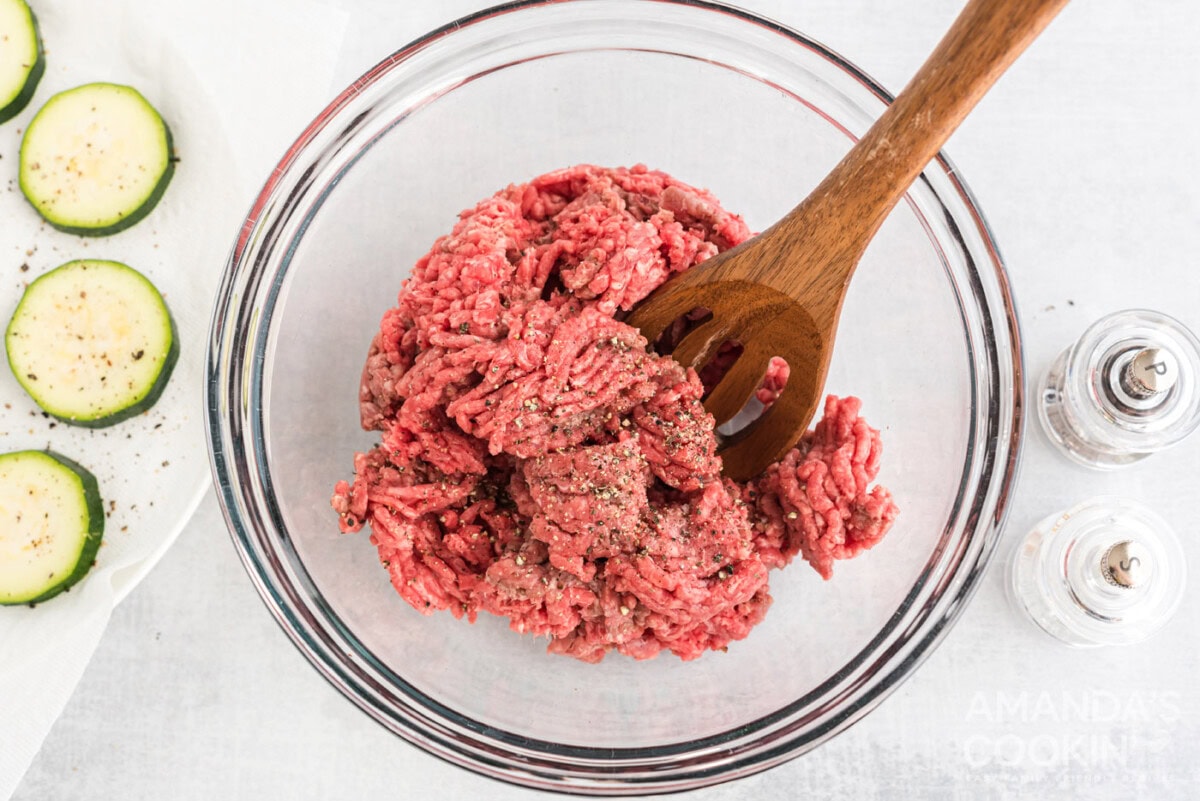 mixing spoon in a bowl of ground beef with salt and pepper