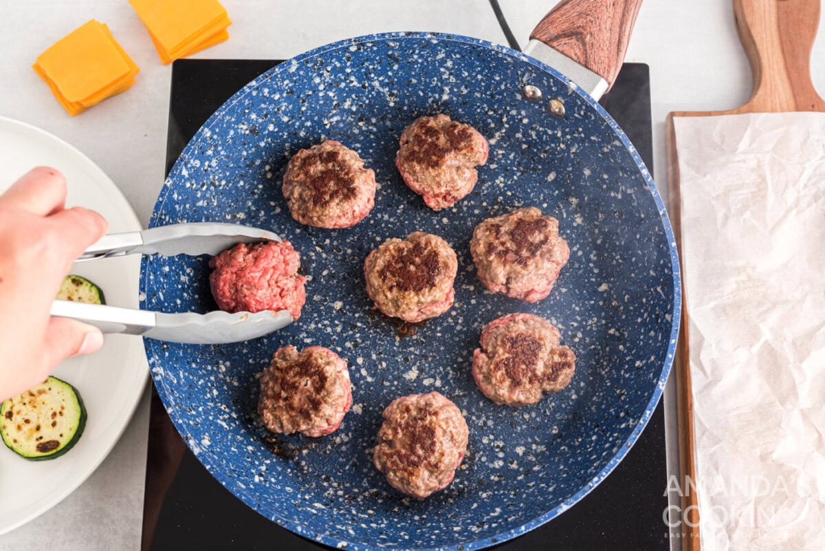 tongs flipping burger patty in a skillet