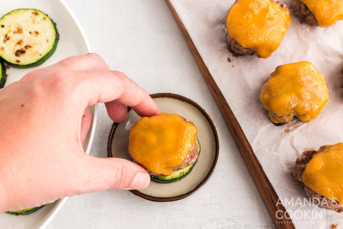 hand placing cheeseburger on zucchini round